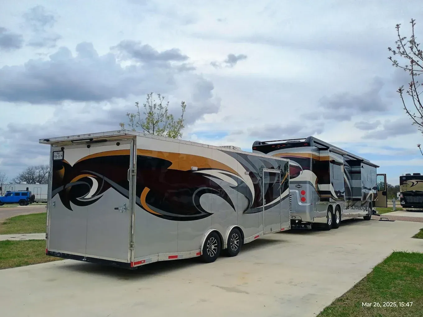 Two large motorhomes parked on a paved lot under a cloudy sky