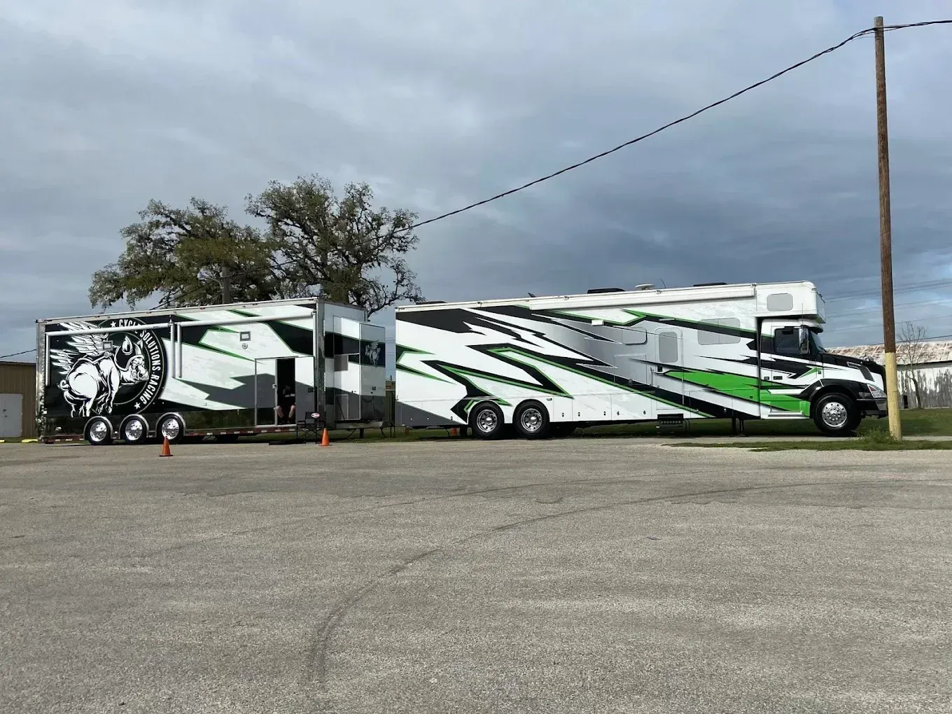 White and green RV motorhome parked on a gravel lot under cloudy sky