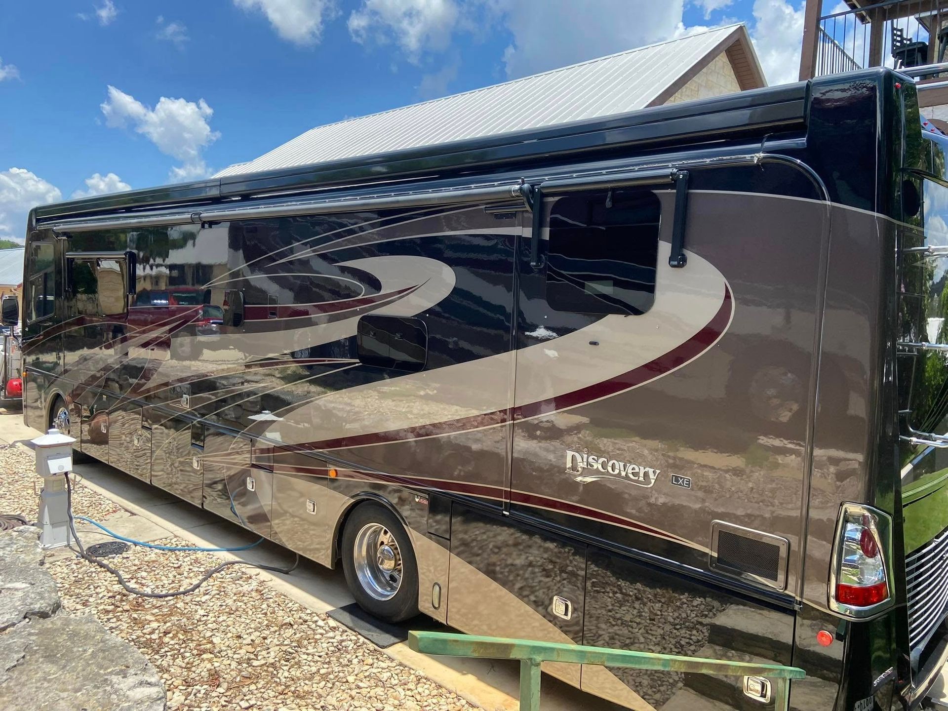 Black motorhome parked outdoors on a sunny day, reflecting the sky and surroundings.