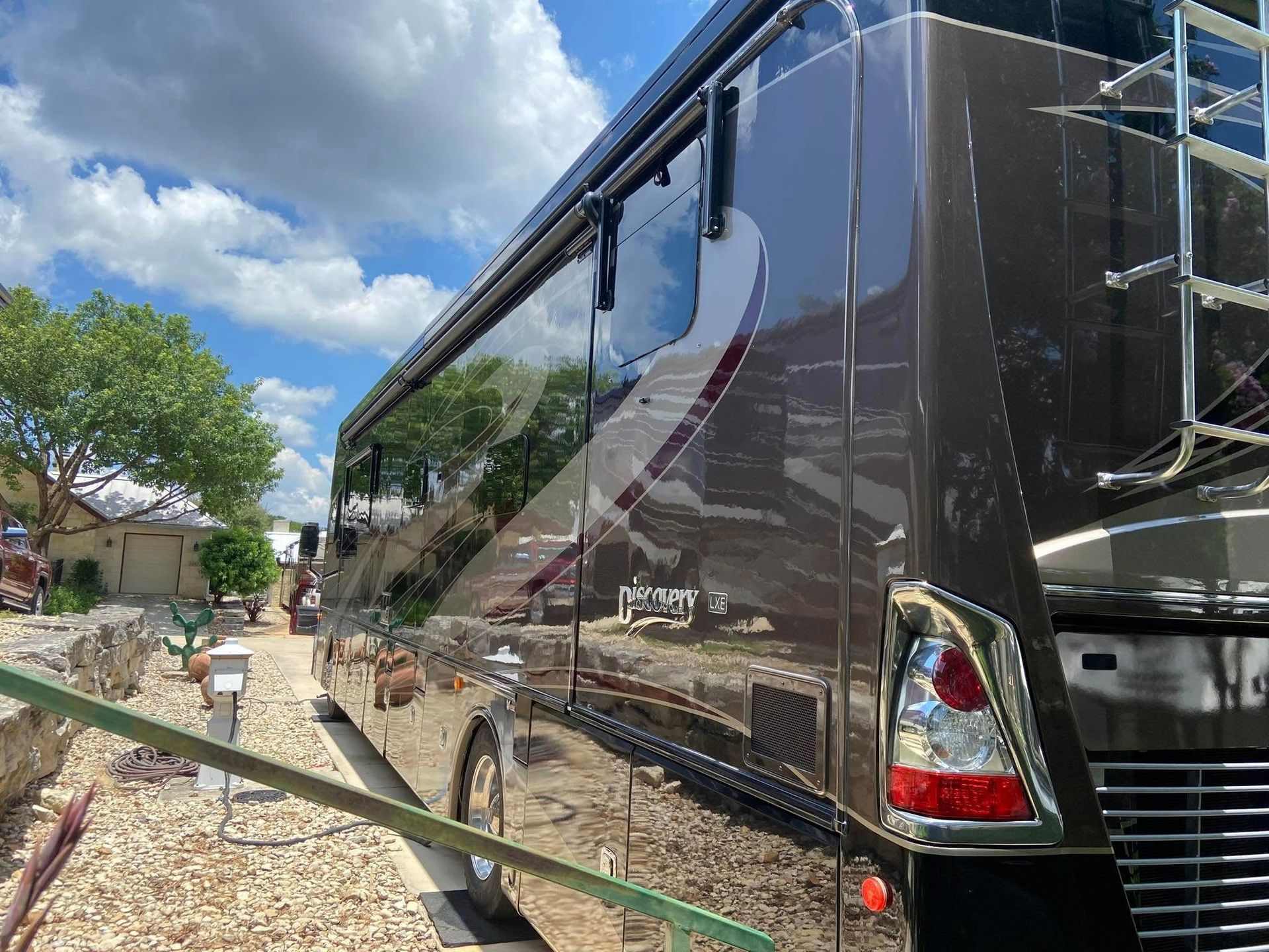 Black coach bus parked on a dirt roadside under a cloudy sky, with trees and small houses nearby