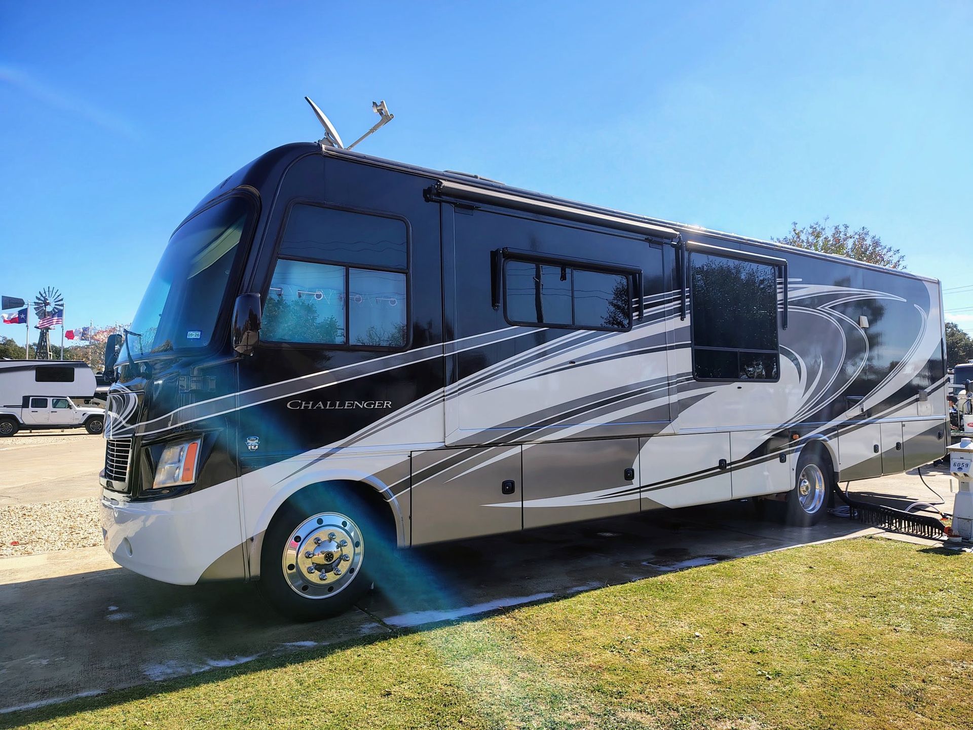 Large silver and black RV parked on grass under a clear blue sky