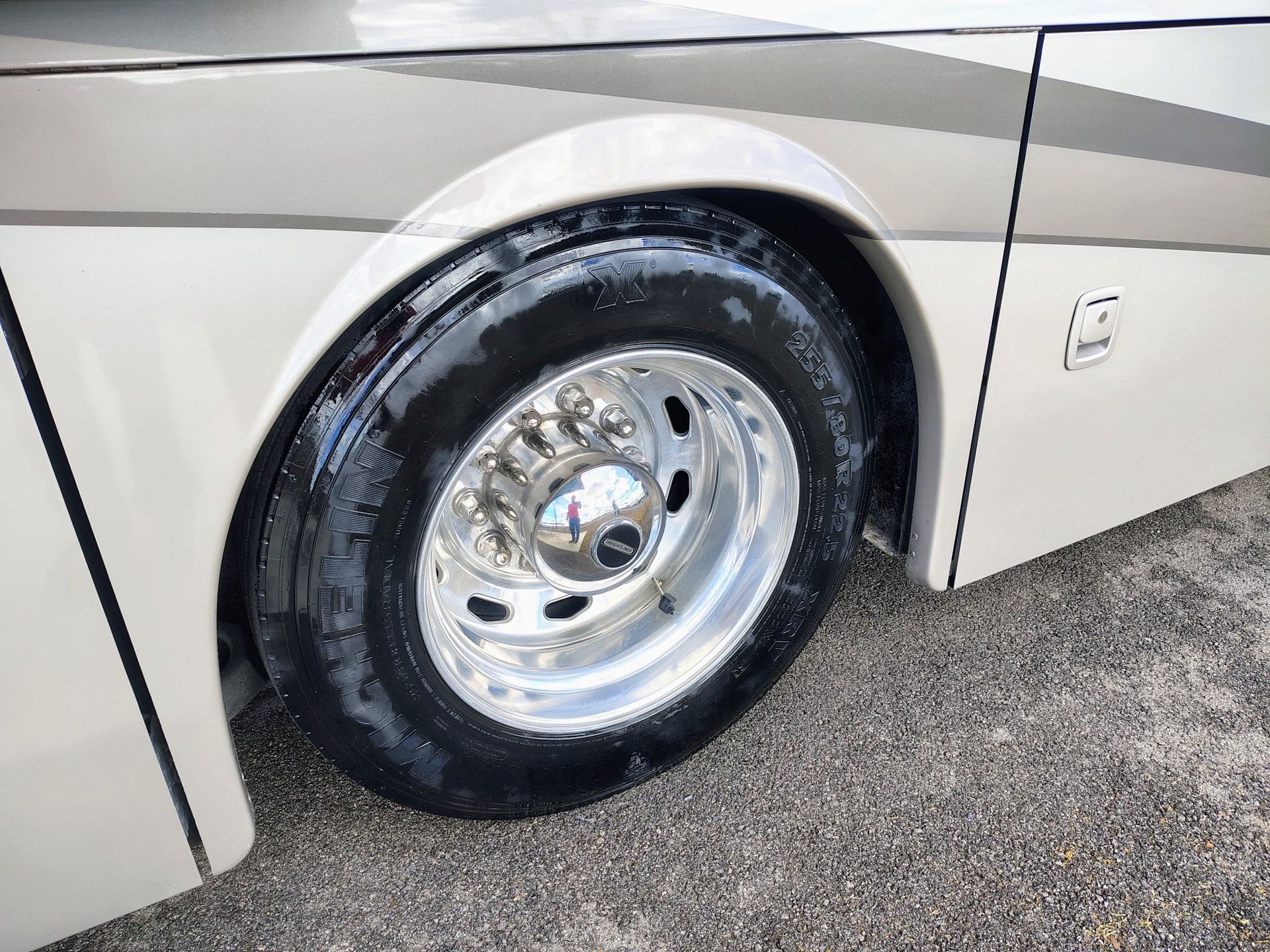 Close-up of a white vehicle’s front wheel with a shiny chrome rim on asphalt.