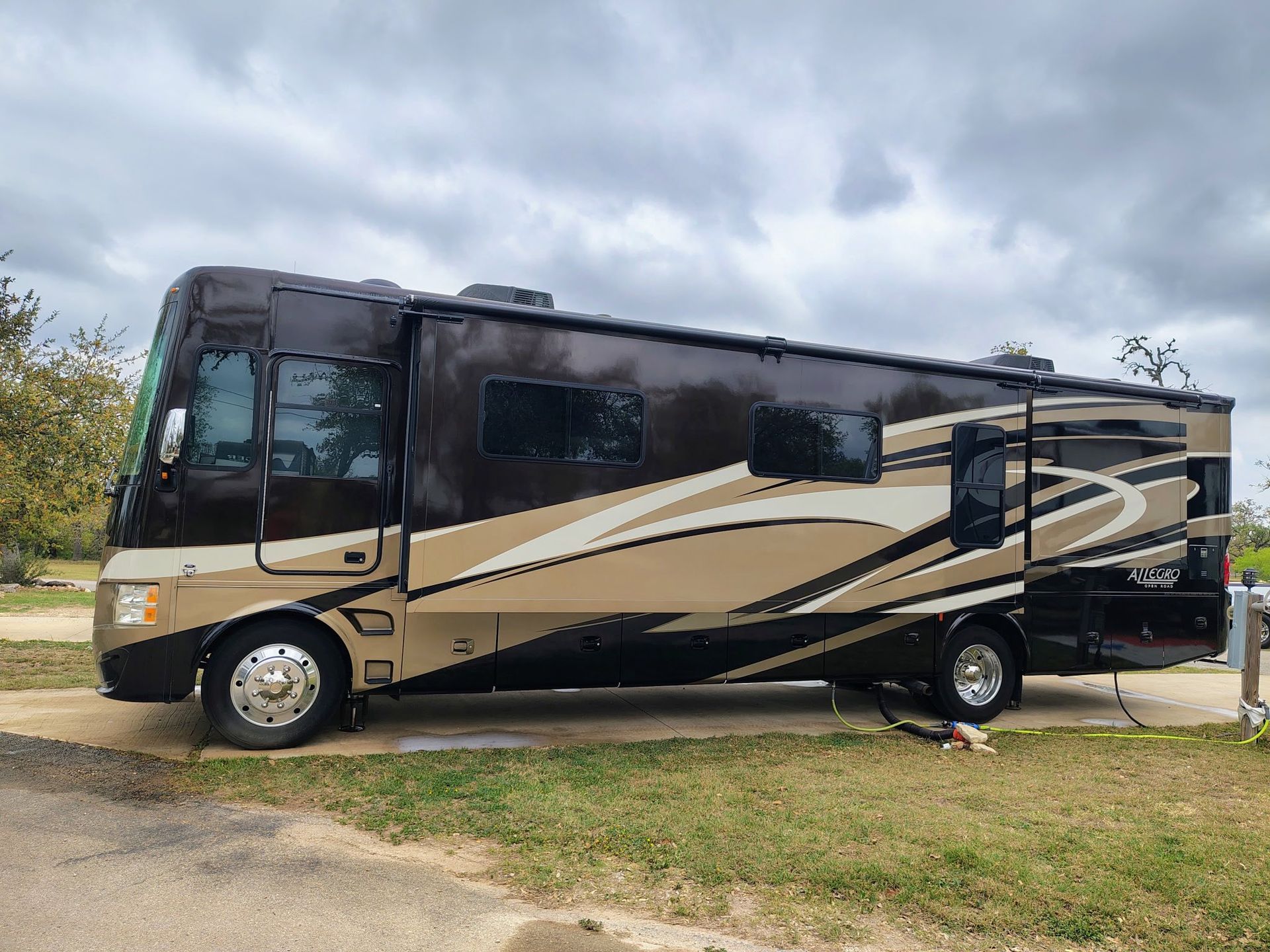 Beige and black motorhome parked on grass under a cloudy sky.