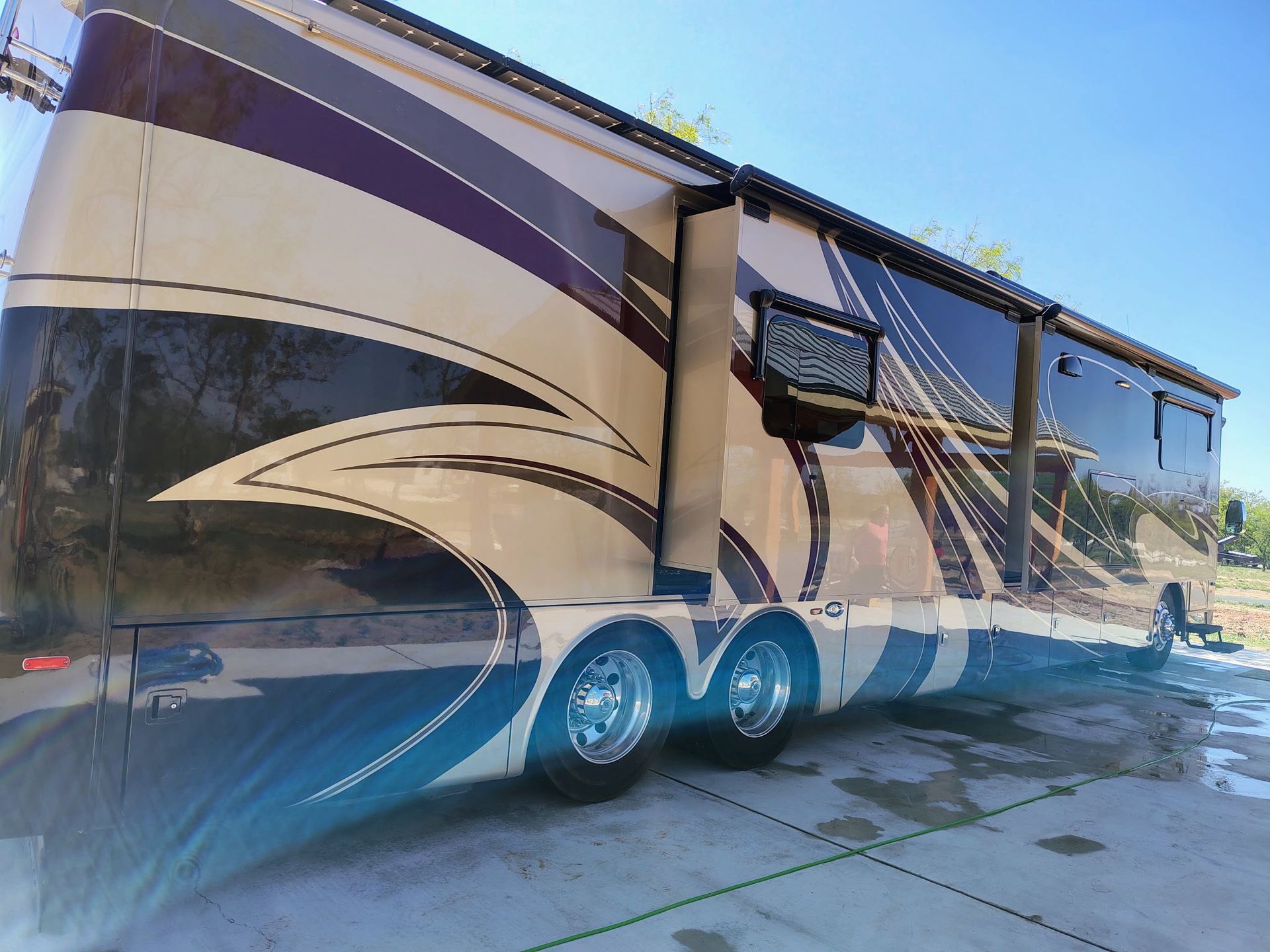 Large beige and brown RV parked on a sunny paved lot, side view with slide-outs extended