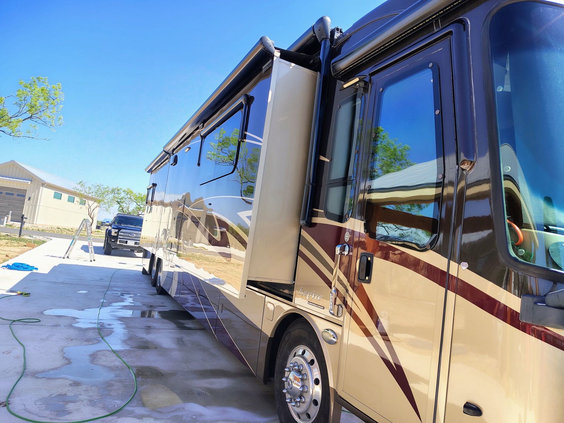 Large beige RV parked in a driveway on a sunny day, with a car and houses in the background