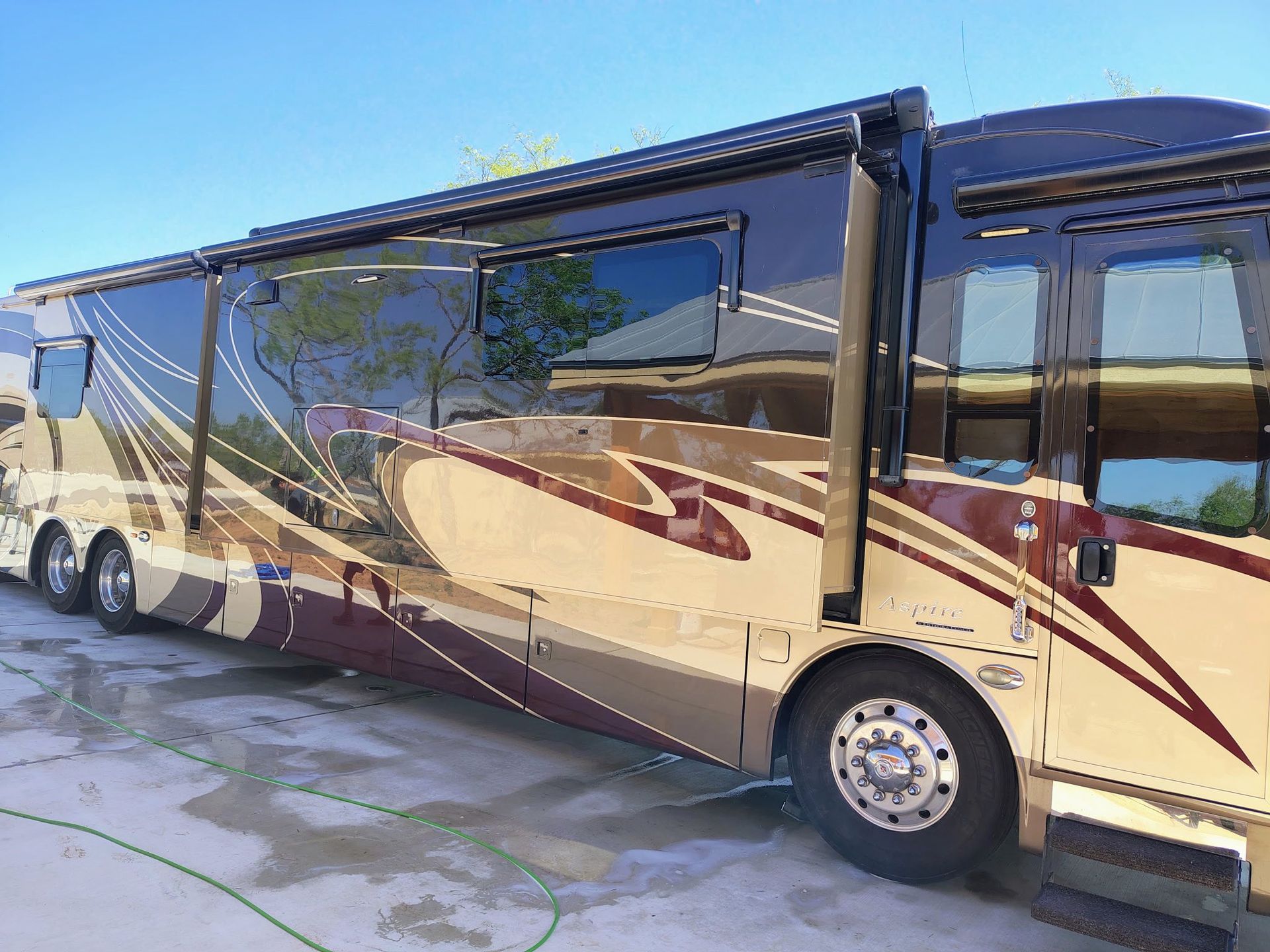 Large beige and maroon luxury RV parked outdoors in bright sunlight
