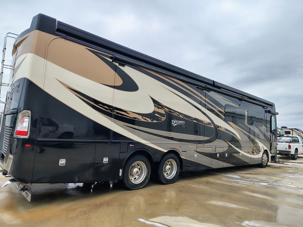 Large beige and black motorhome RV parked on a wet lot under cloudy skies