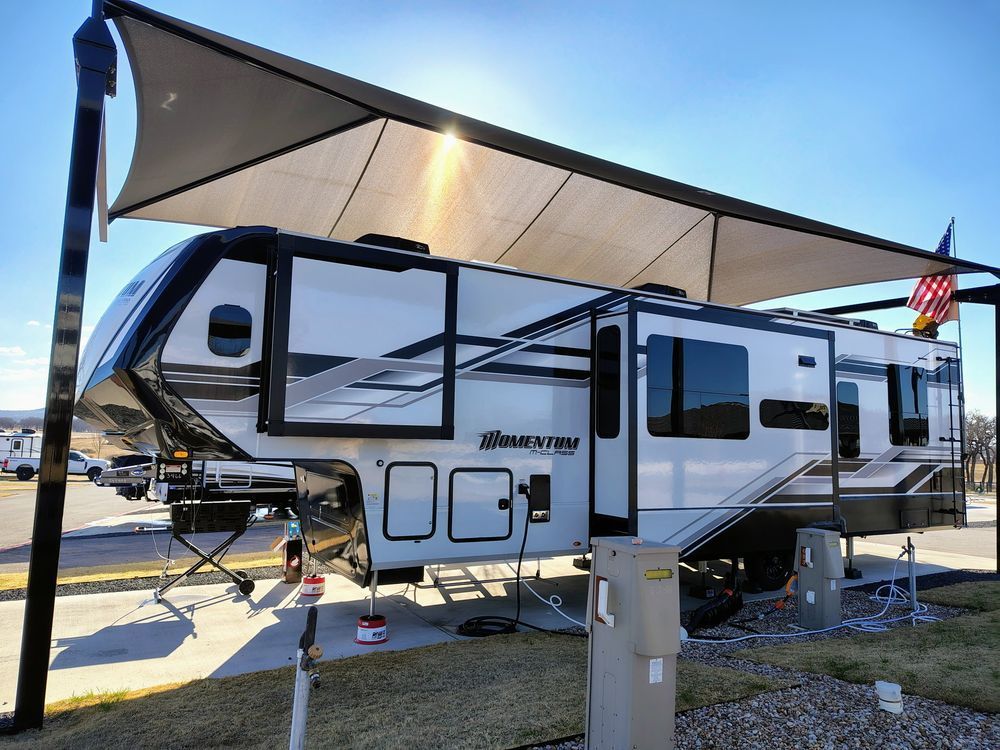 White and black travel trailer with awning extended at an RV campsite in bright sunlight