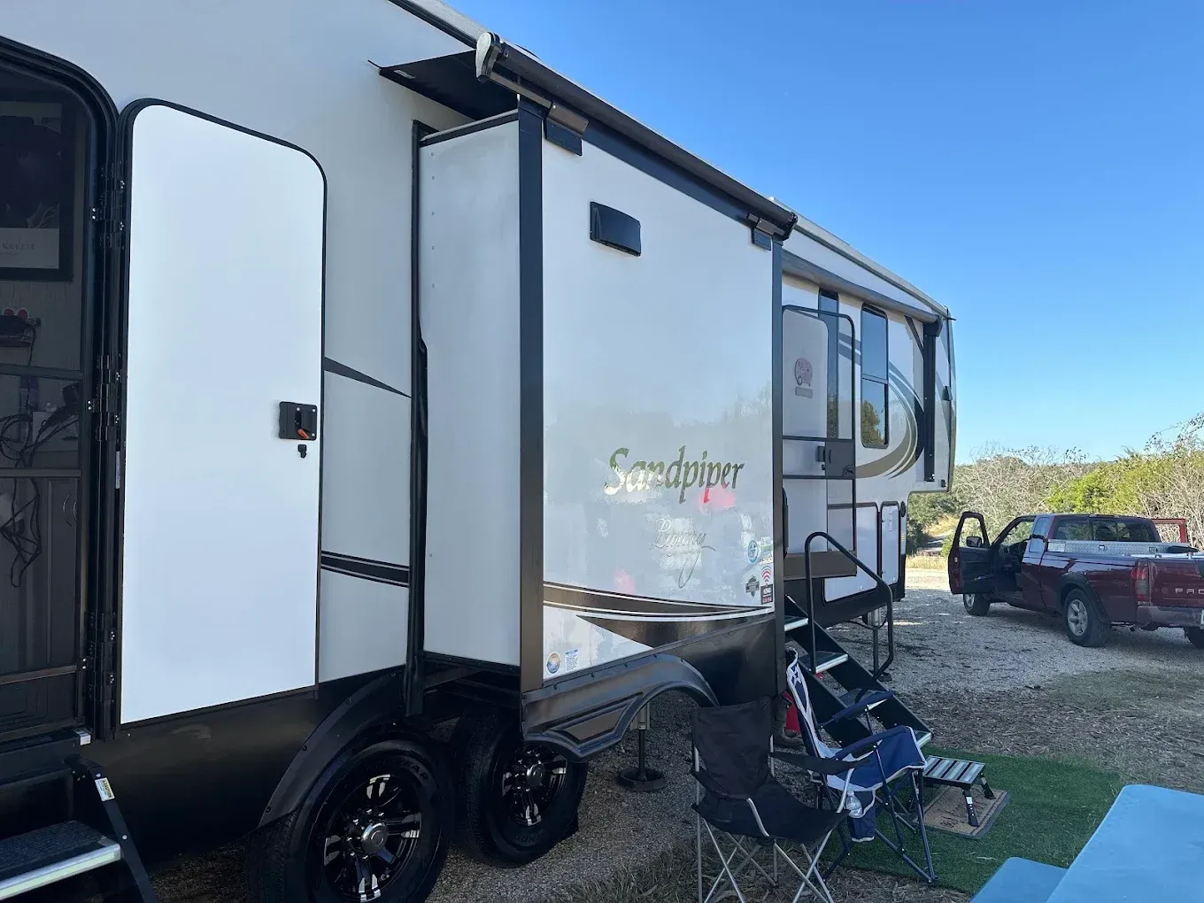 White travel trailer with slide-out parked on grass beside a truck under a clear blue sky