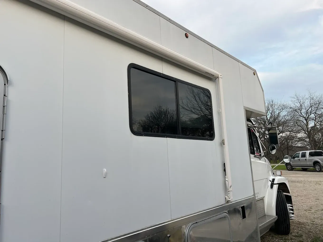 White box truck with a side window parked outdoors on a cloudy day