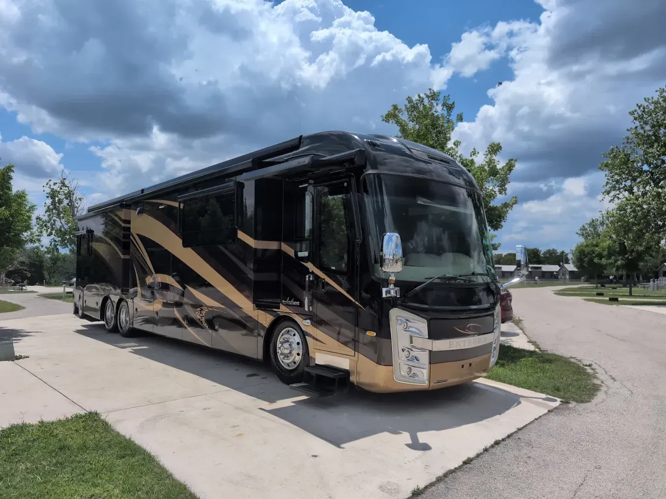 Black and gold motorcoach parked on a paved lot under a partly cloudy sky.