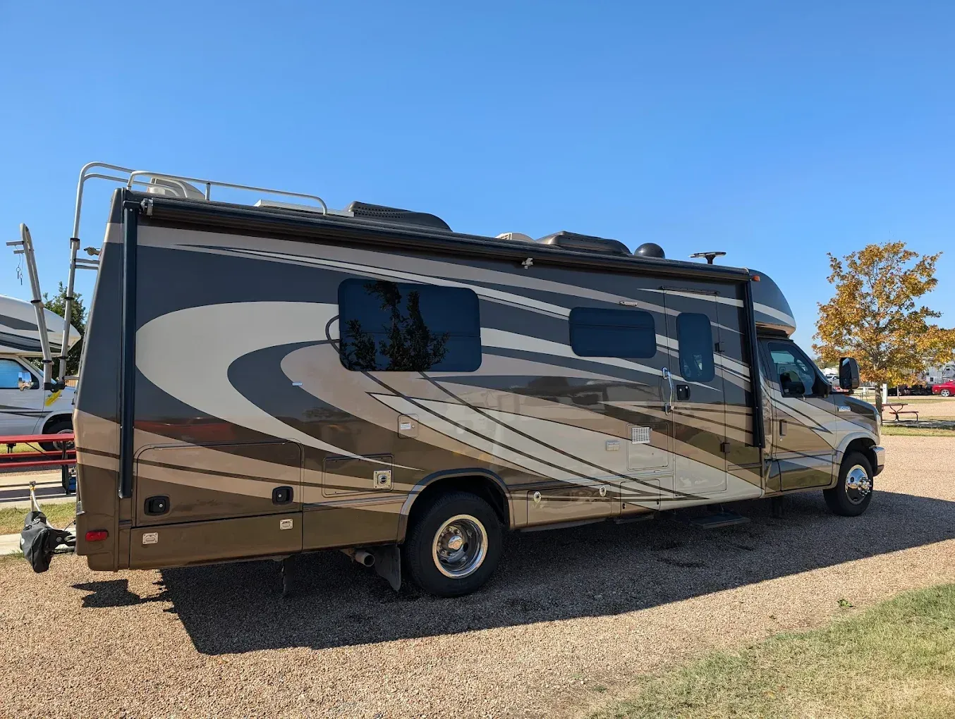 Brown and tan RV parked on gravel under a clear blue sky