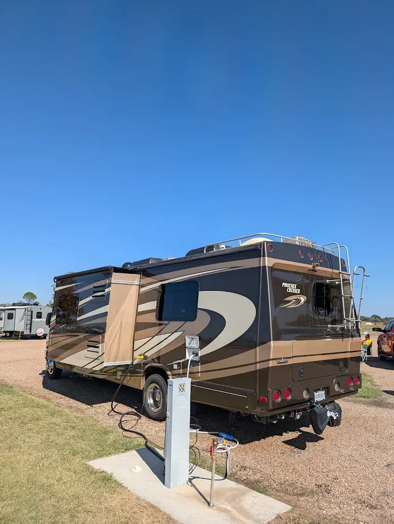 Tan and brown RV parked on grass under a clear blue sky, with another vehicle in the background.