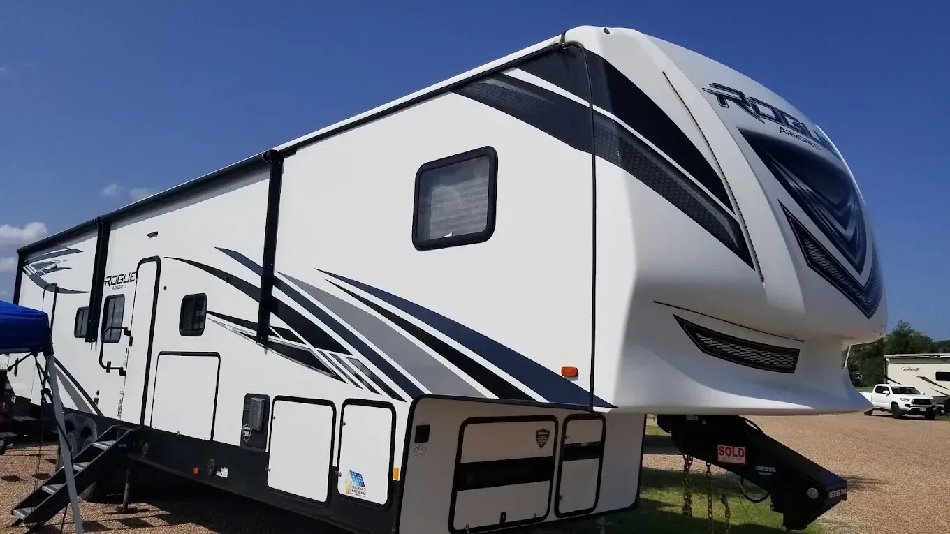 White fifth-wheel RV trailer with black and blue graphics parked outdoors under a clear sky