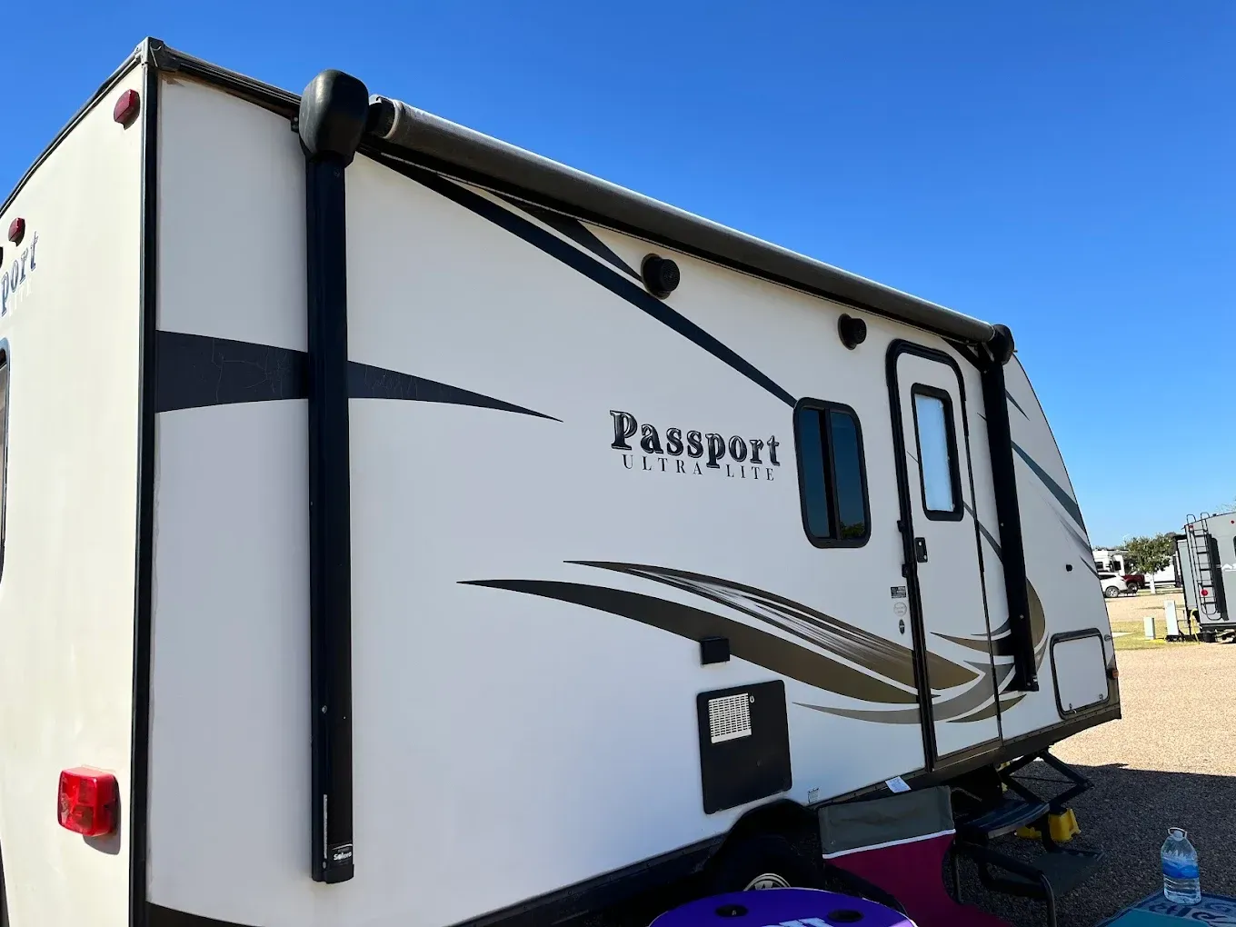 White Passport RV trailer with black trim parked outdoors under a blue sky.