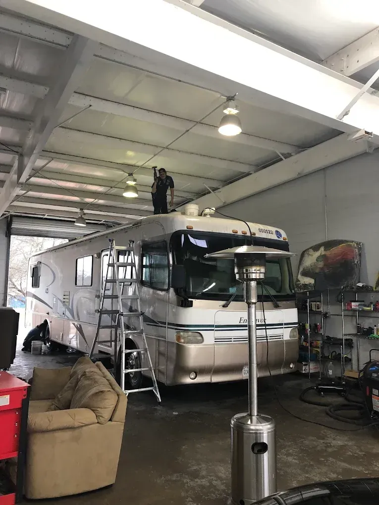 RV parked inside a garage with a couch, ladders, and tools around it