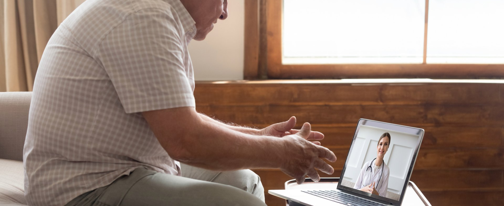 Man sitting on a couch video chatting on a laptop by a sunlit window