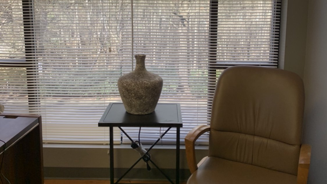 Living room with a patterned vase on a small black table beside a tan leather chair in front of blinds