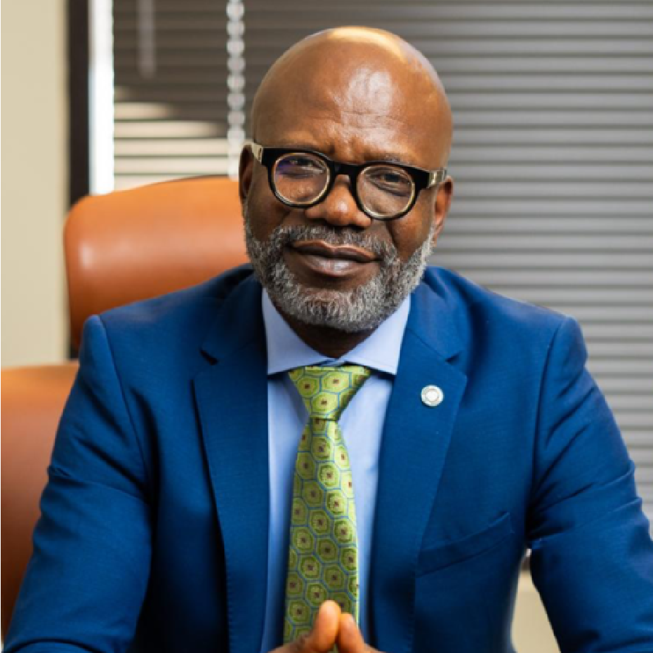 Man in blue suit, glasses, and green patterned tie, seated in an office, smiling.