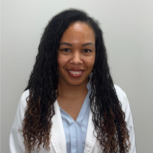 Woman in a white lab coat and light blue shirt, smiling against a plain white background.