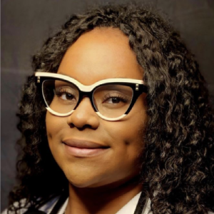 Woman with curly hair and glasses, smiling.