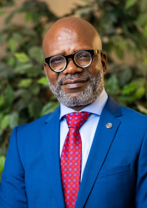 Man in blue suit, glasses, and red tie, facing forward, with a slight smile.