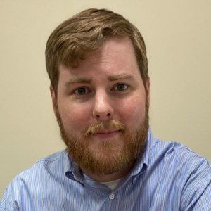 Man with a red beard and blue striped shirt, looking at the camera. Neutral background.
