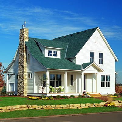 White suburban house with green roof, stone chimney, and landscaped front yard under a blue sky