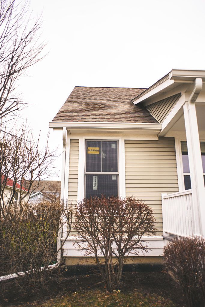 House exterior with beige siding, small porch, and shrubs in front, viewed on a cloudy day