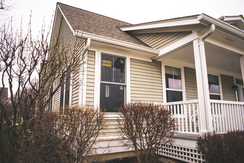 Front porch of a beige house with white trim and leafless shrubs in front