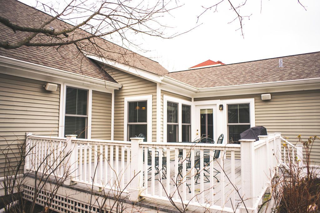 White porch on a beige house with windows, railing, and bare winter branches