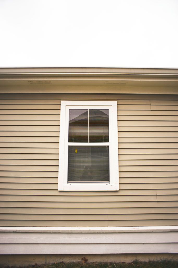 Beige house siding with a white-framed window centered on the wall.