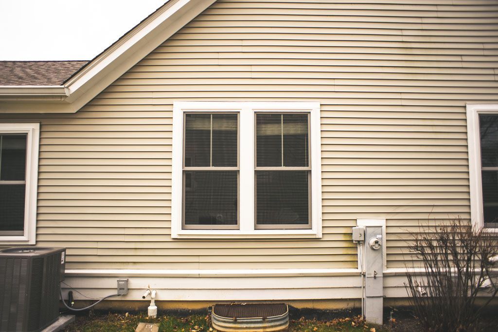 Beige house exterior with two white-framed windows and a sloped roof eave.