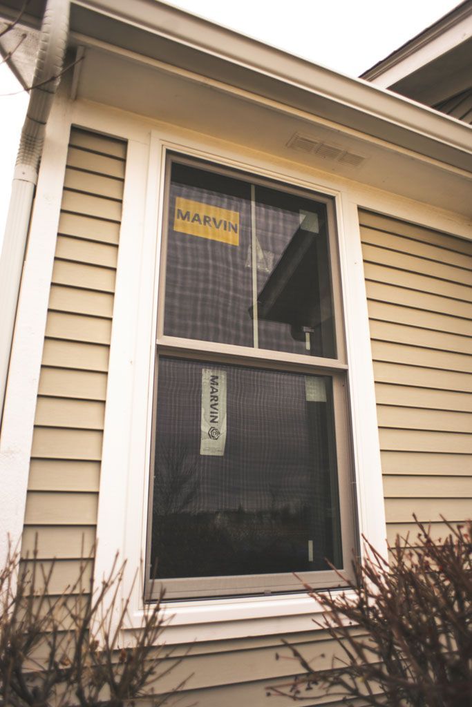 Two-story house window with trim, showing a dark screen and a yellow sign inside