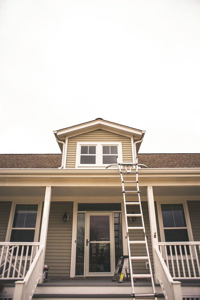 House front with a ladder leaning to the roof, centered above the porch entrance