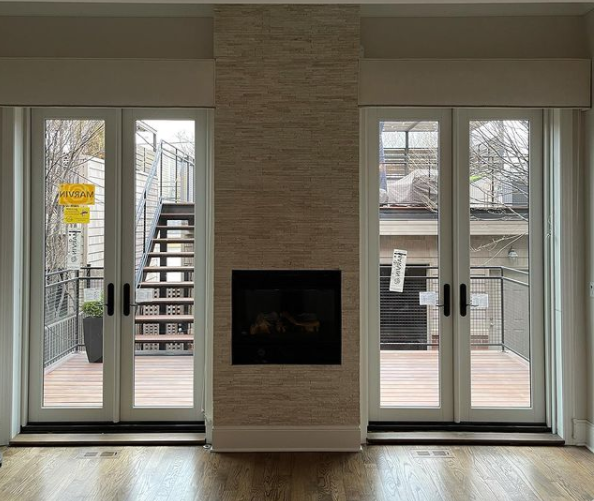Modern living room with central fireplace, white sliding glass doors, and deck view