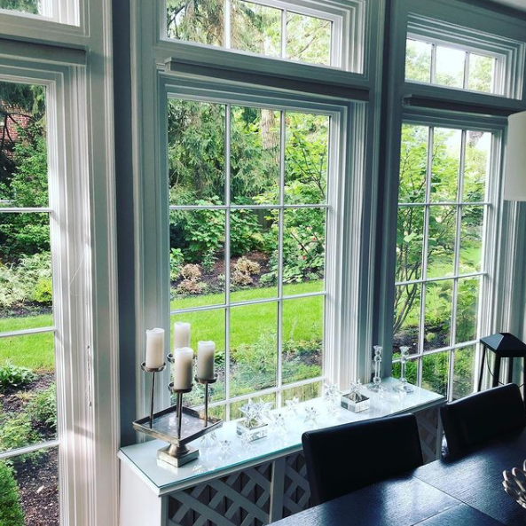 Dining room table by large windows overlooking a green garden, with candles and black chairs