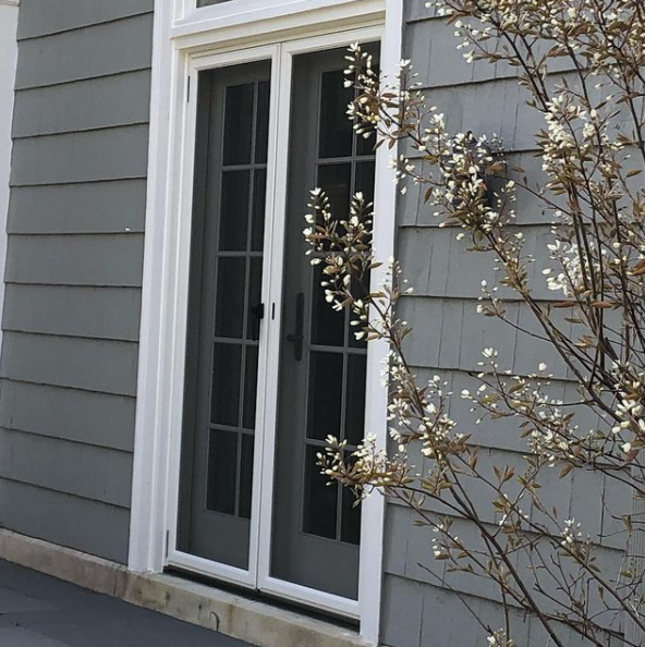 White French doors on a gray house exterior with a shrub beside them