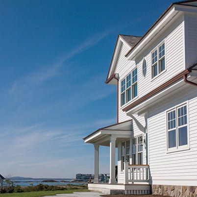 White seaside house with porch and blue sky overlooking water