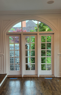 Elegant French doors with arched transom windows opening to a lush garden and terrace.