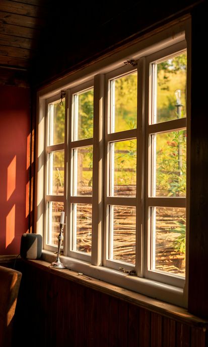 Sunlit wooden window with multiple panes, casting warm light onto a red interior wall