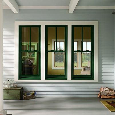 Green-trimmed porch window wall with white siding, benches, and baskets on a covered front porch.