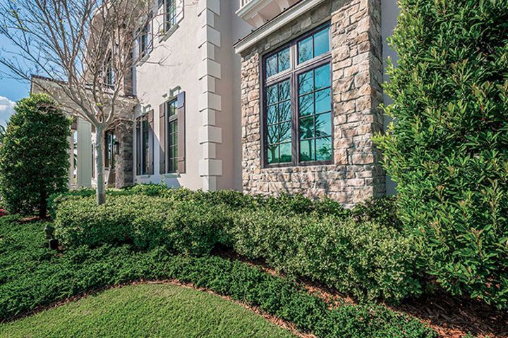 Stone building exterior with large blue windows, manicured hedges, and a green lawn