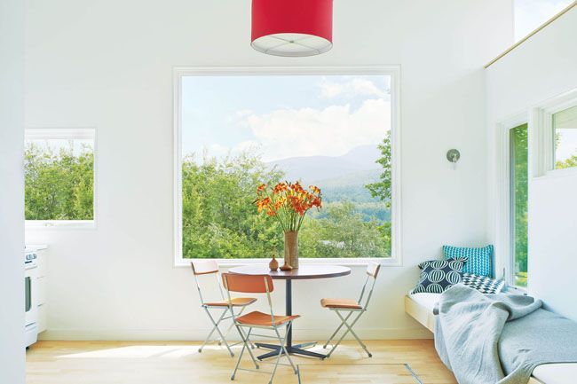 Bright white room with large window, small table and chairs, and a blue daybed with pillows