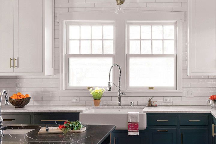 Bright kitchen with white brick walls, double windows, a sink, and dark blue cabinets beneath the counter.