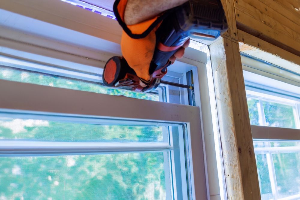Worker installing window trim indoors with a power tool and orange safety harness