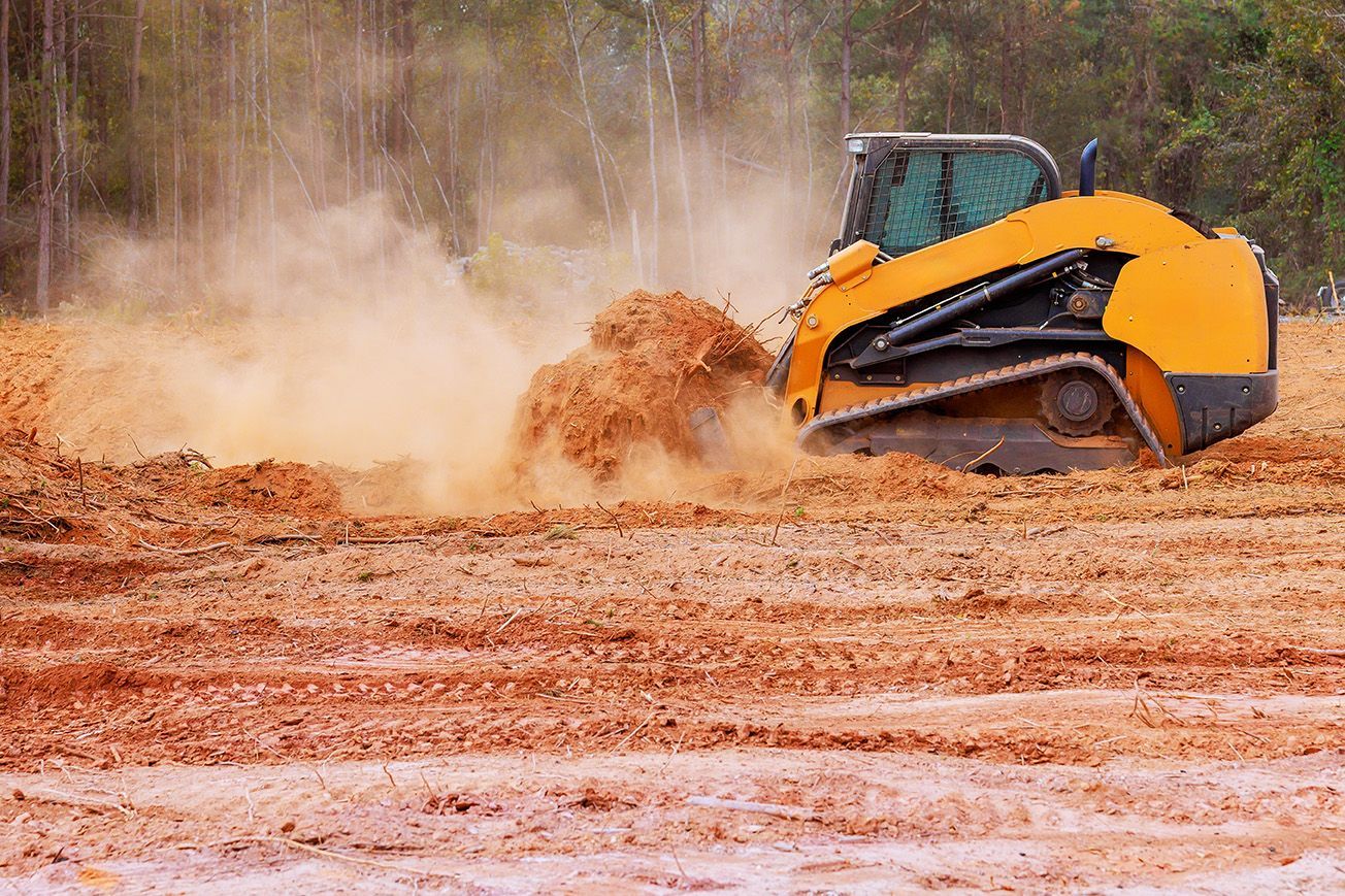 A yellow skid steer loader moves dirt on a construction site, creating a cloud of dust.