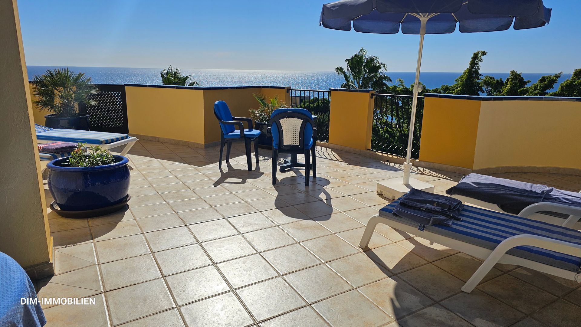 Ein Balkon mit Tisch und Stühlen und einem Sonnenschirm mit Blick auf das Meer