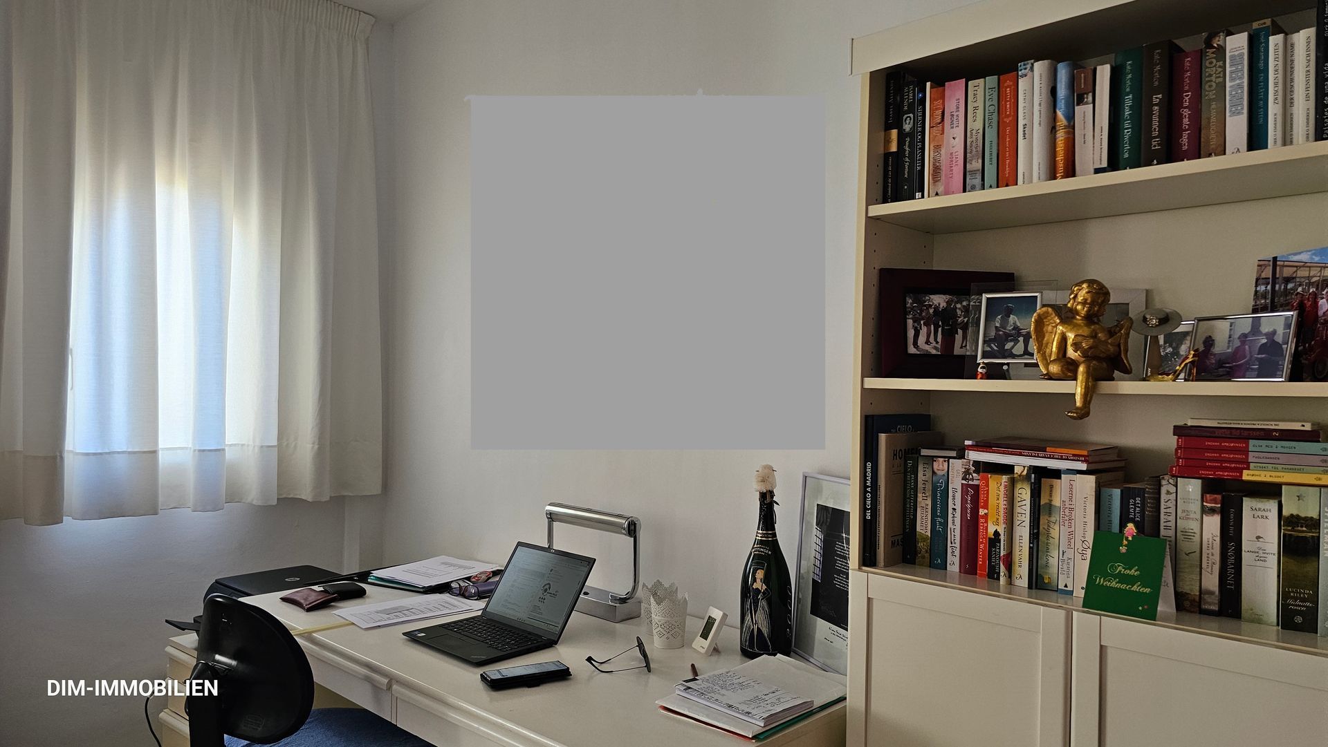 Ein Schreibtisch mit einem Laptop darauf in einem Raum mit einem Bücherregal voller Bücher.