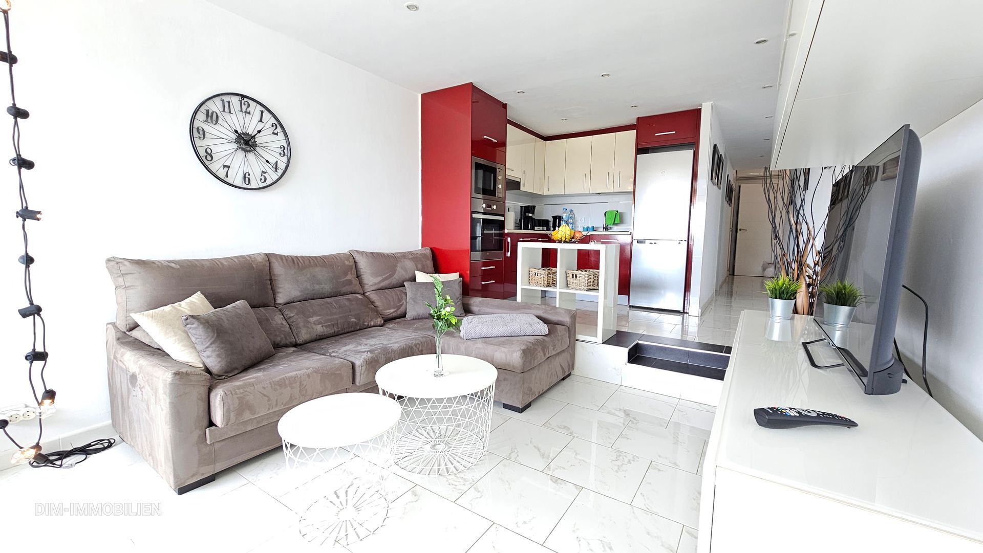 Ein Wohnzimmer mit Couch, Fernseher und einer Uhr an der Wand.